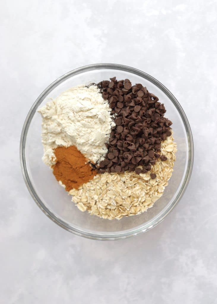 Oats, chocolate chips, flour, and cinnamon in glass bowl