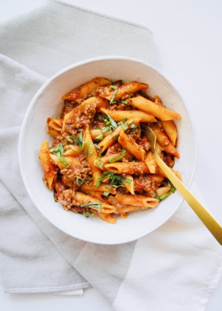 Penne Bolognese in white bowl with gold fork