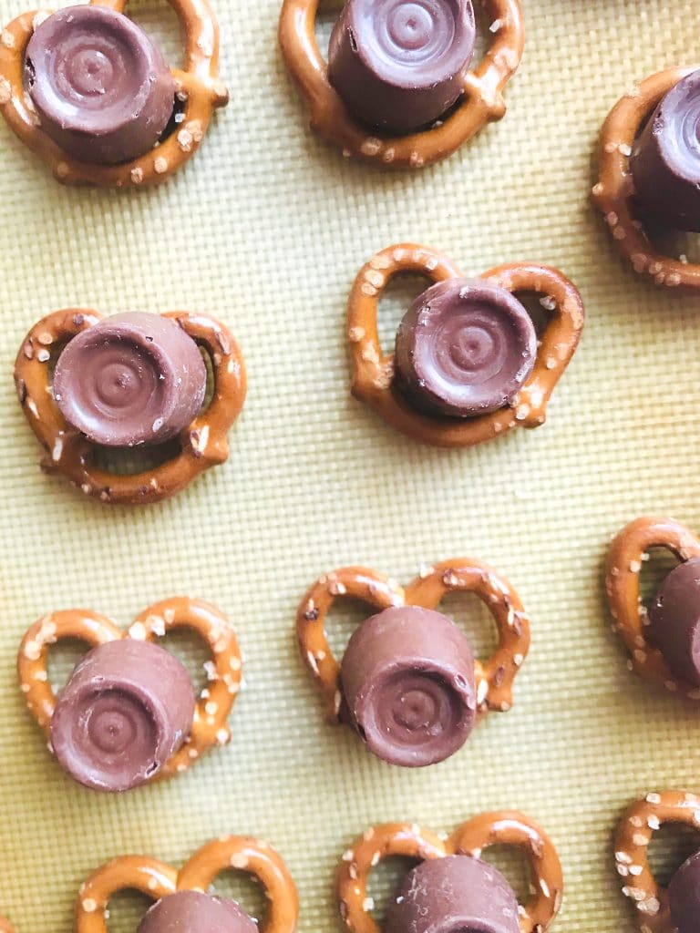 Rolos on top of pretzels on a silicone mat lined baking sheet