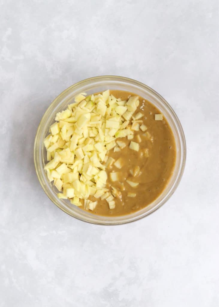 Cake batter with chopped apples in glass bowl