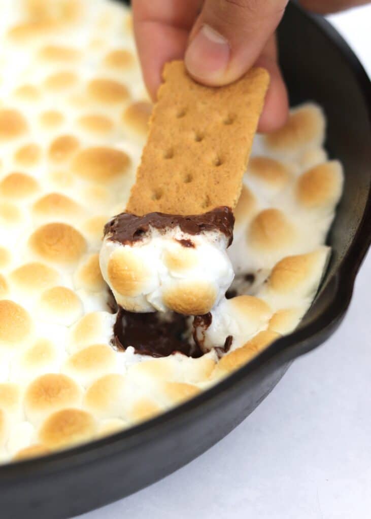 Graham cracker dipping into melted chocolate and toasted marshmallow