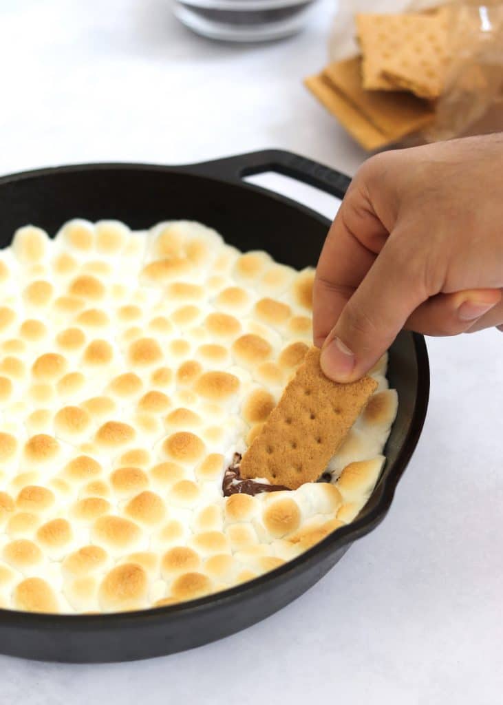 Hand dipping graham cracker into s'mores dip