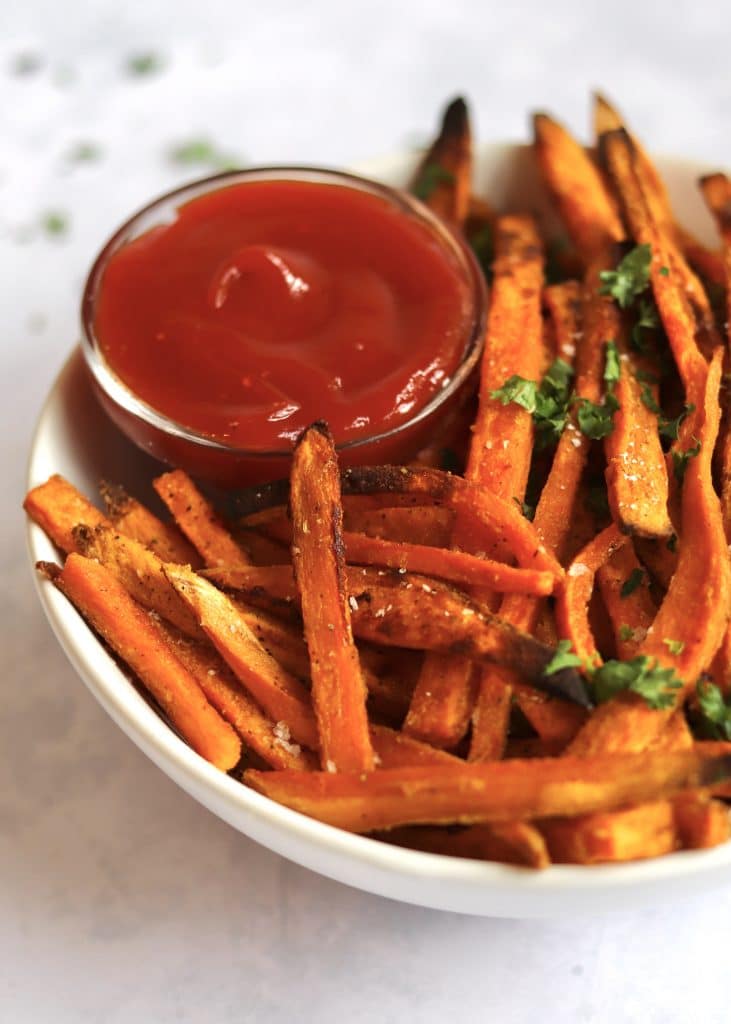 Crispy sweet potato fries in a bowl with fresh parsley