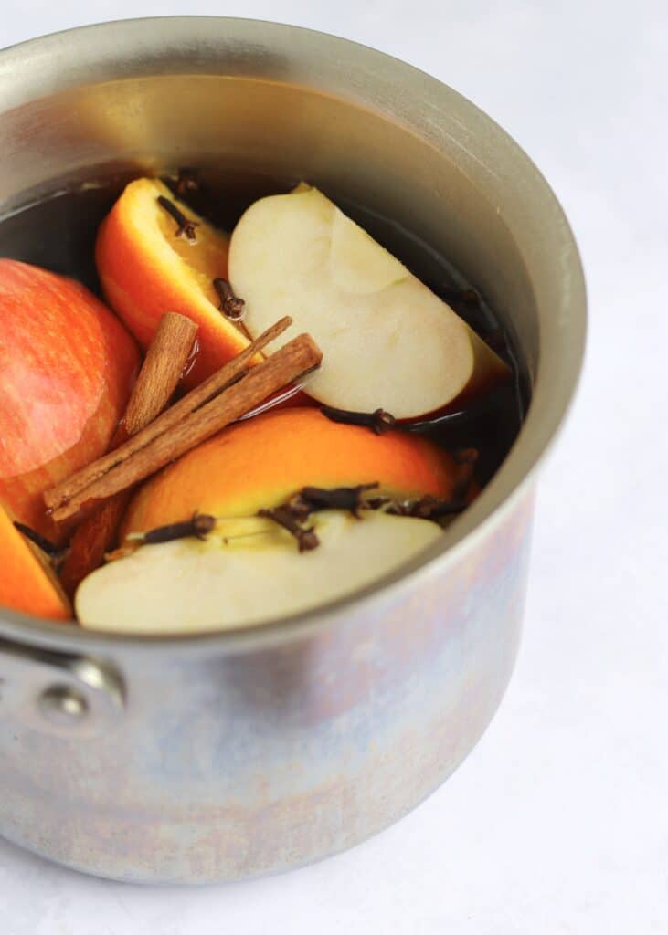 Apples, orange, cinnamon sticks, and whole cloves in pot of water