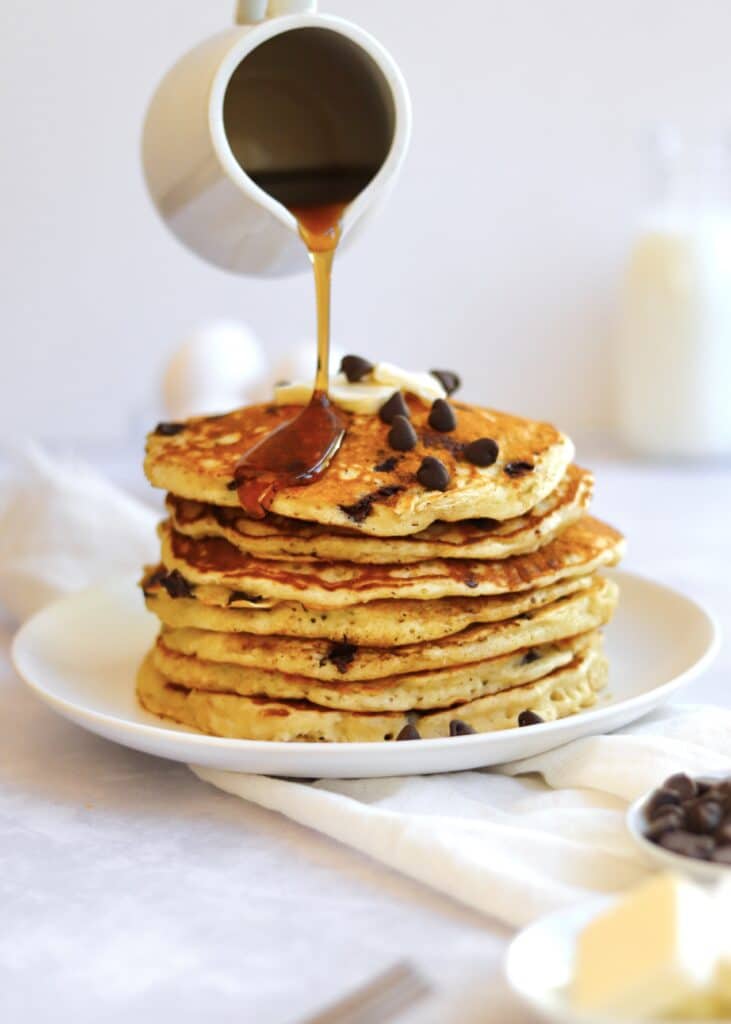 Maple syrup being poured on a stack of fluffy chocolate chip pancakes