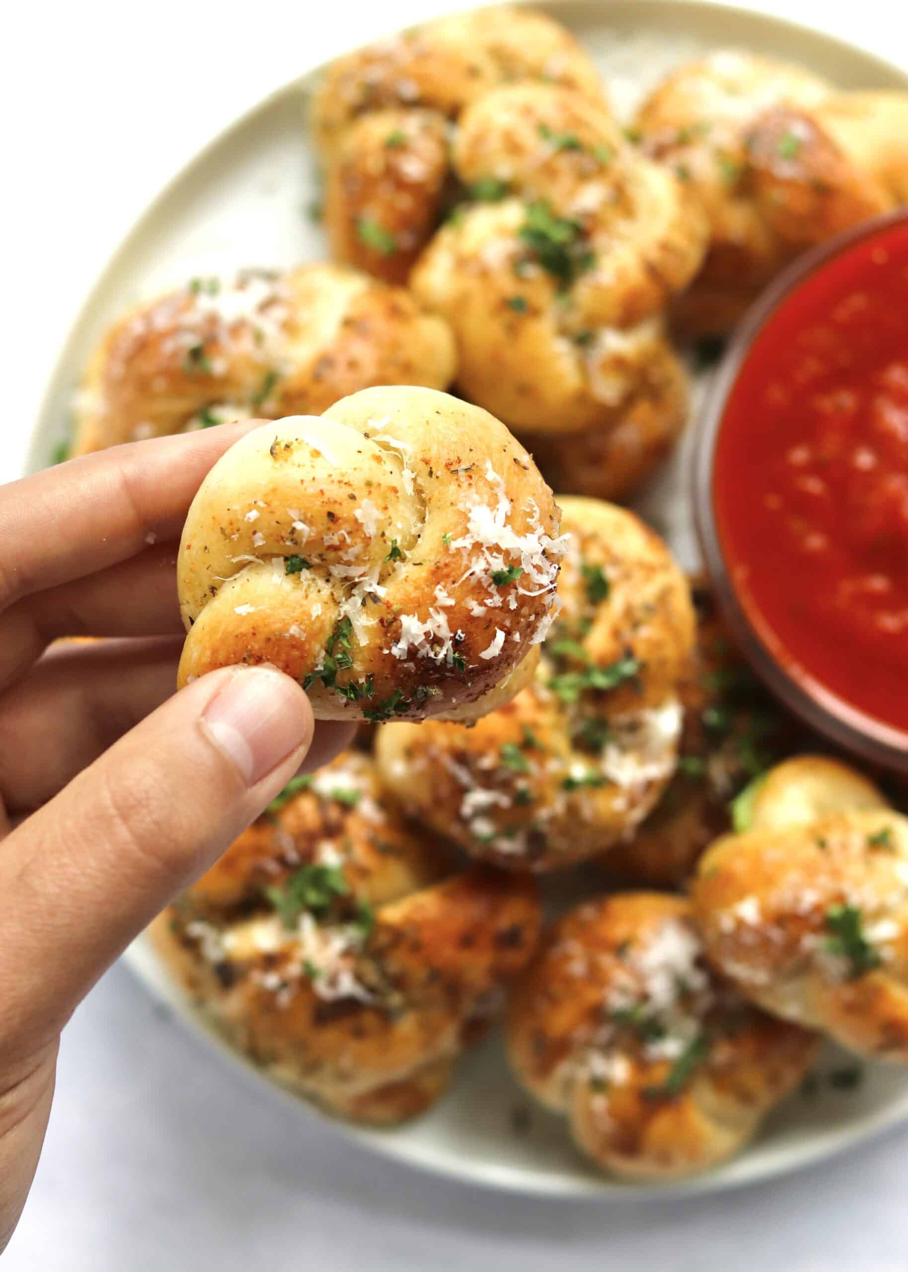hand holding a garlic knot over a full plate