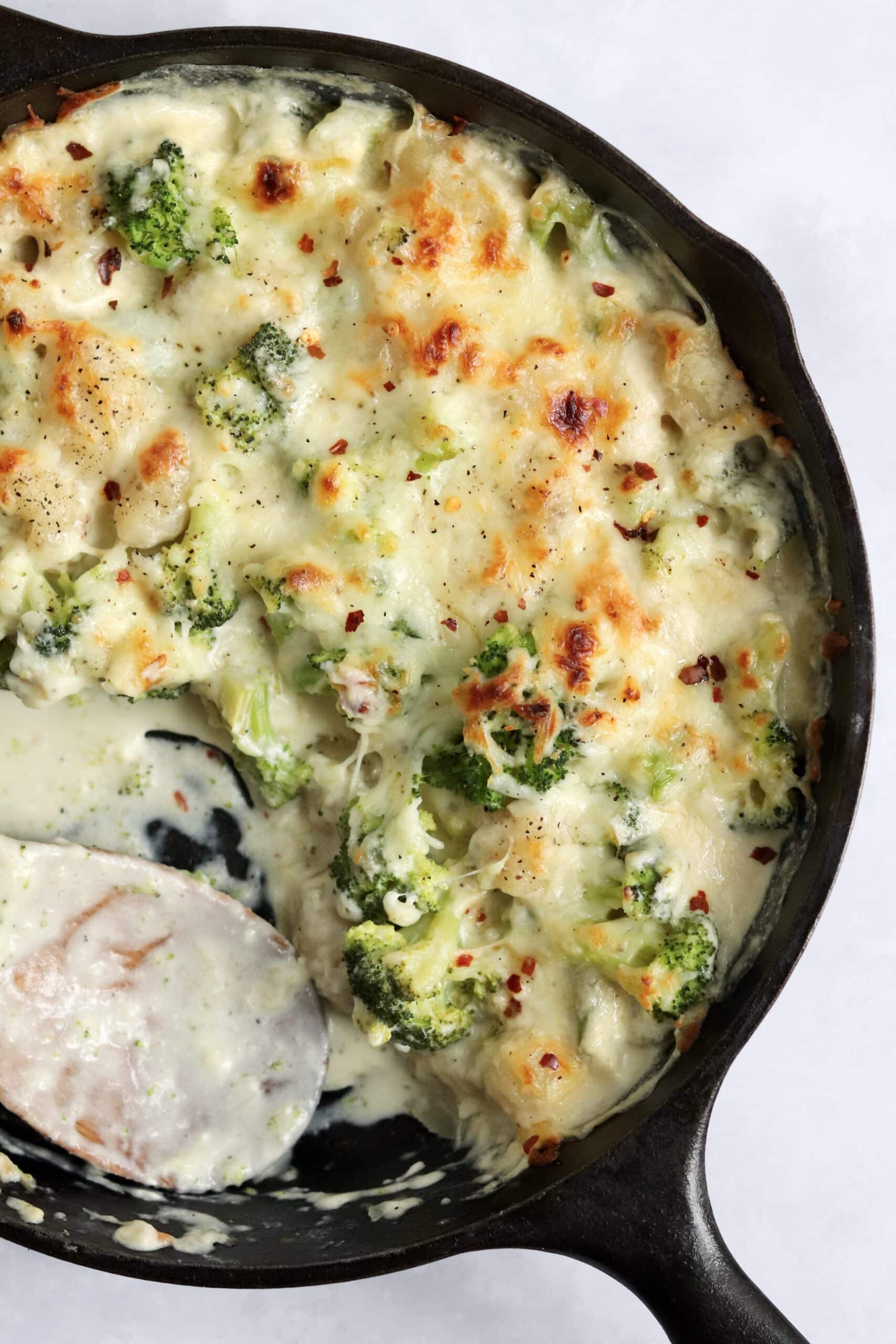 Creamy and cheesy broccoli gnocchi baked in a cast iron skillet with a wooden spoon