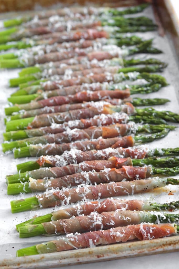 Roasted asparagus wrapped in prosciutto and sprinkled with parmesan cheese on a sheet pan