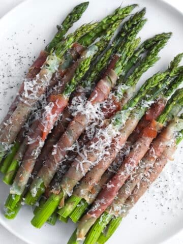 Prosciutto wrapped asparagus on a plate with parmesan cheese