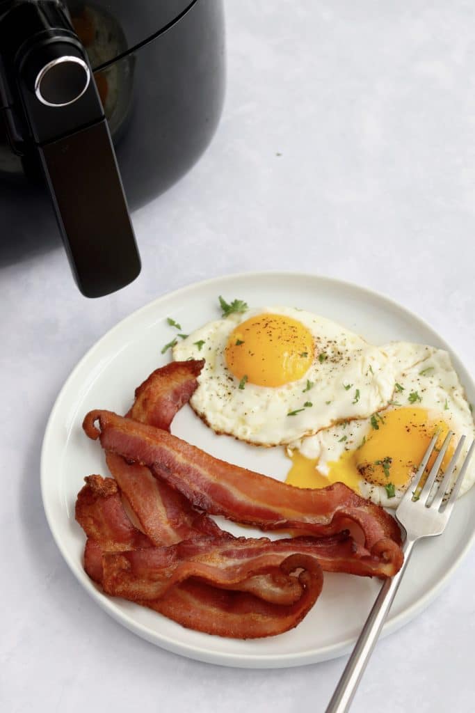 bacon cooked in an air fryer on a plate with eggs
