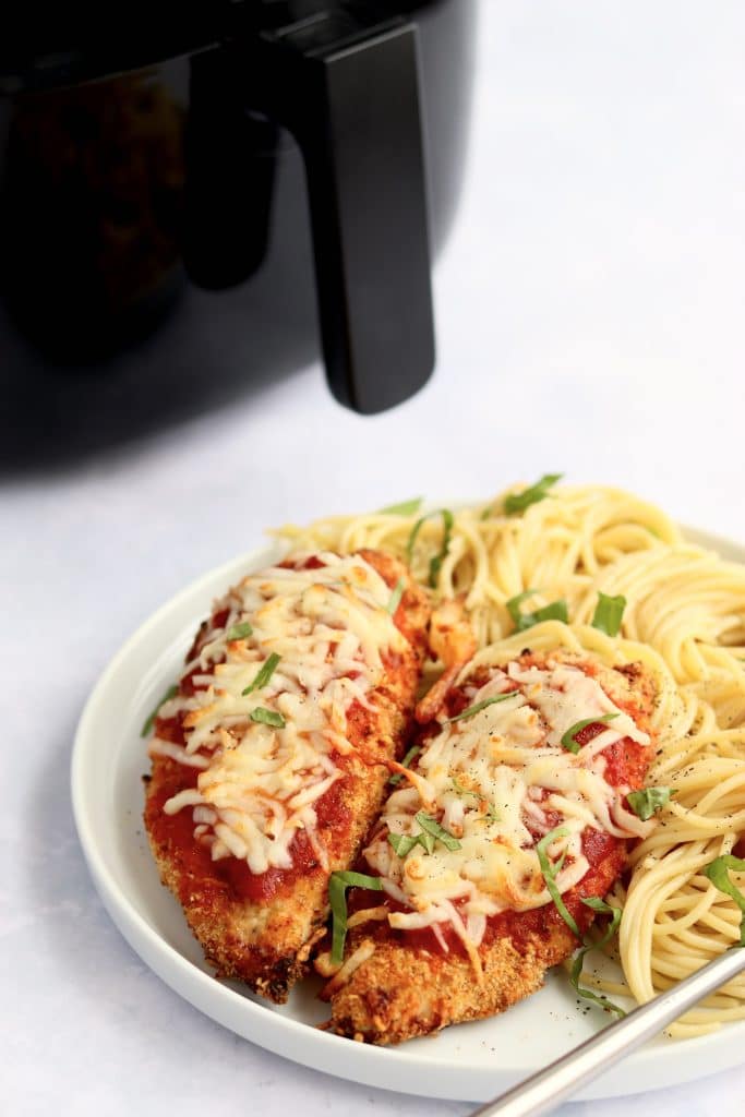 Plate of chicken parmesan and pasta with air fryer in the background