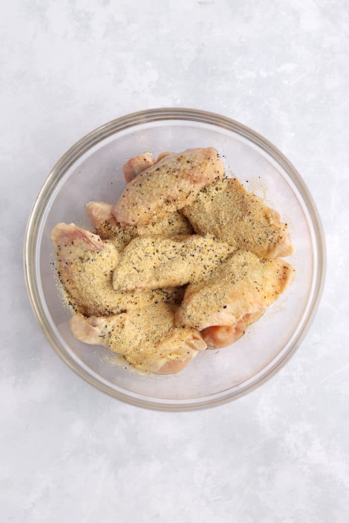 Bowl of raw chicken wings with spices - lemon pepper, garlic powder, and salt