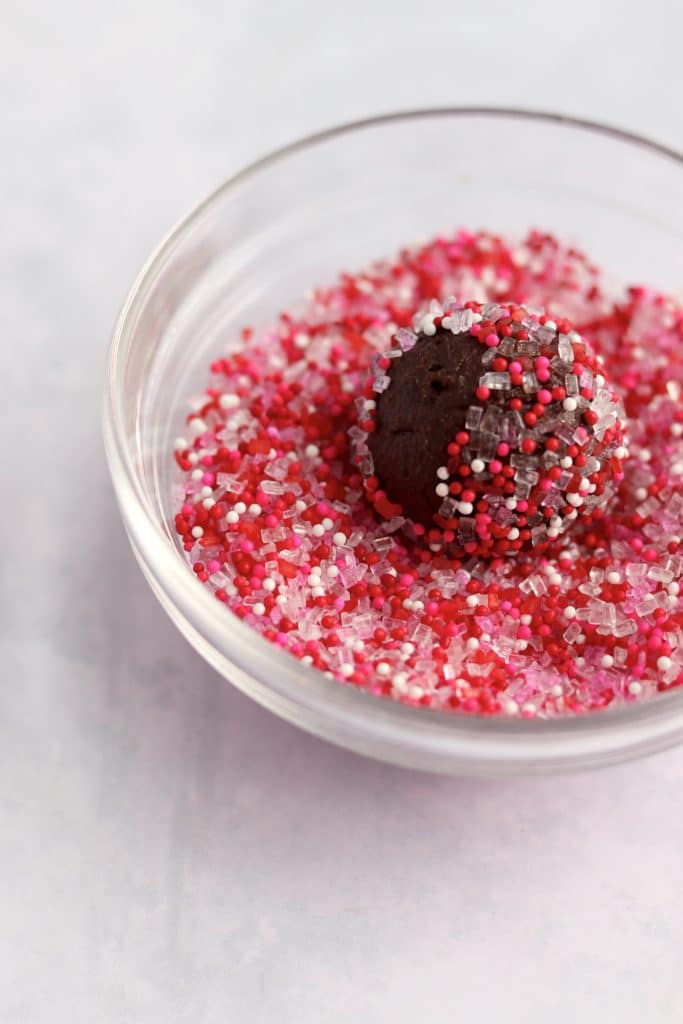 Chocolate truffle being dipped in pink and red sprinkles