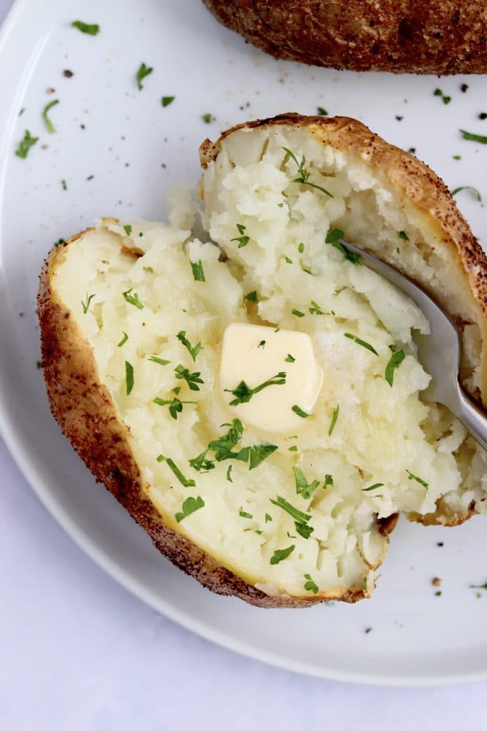Close up of an air fryer baked potato with butter on a plate