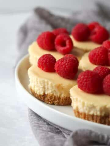 Mini cheesecakes topped with raspberries on a plate
