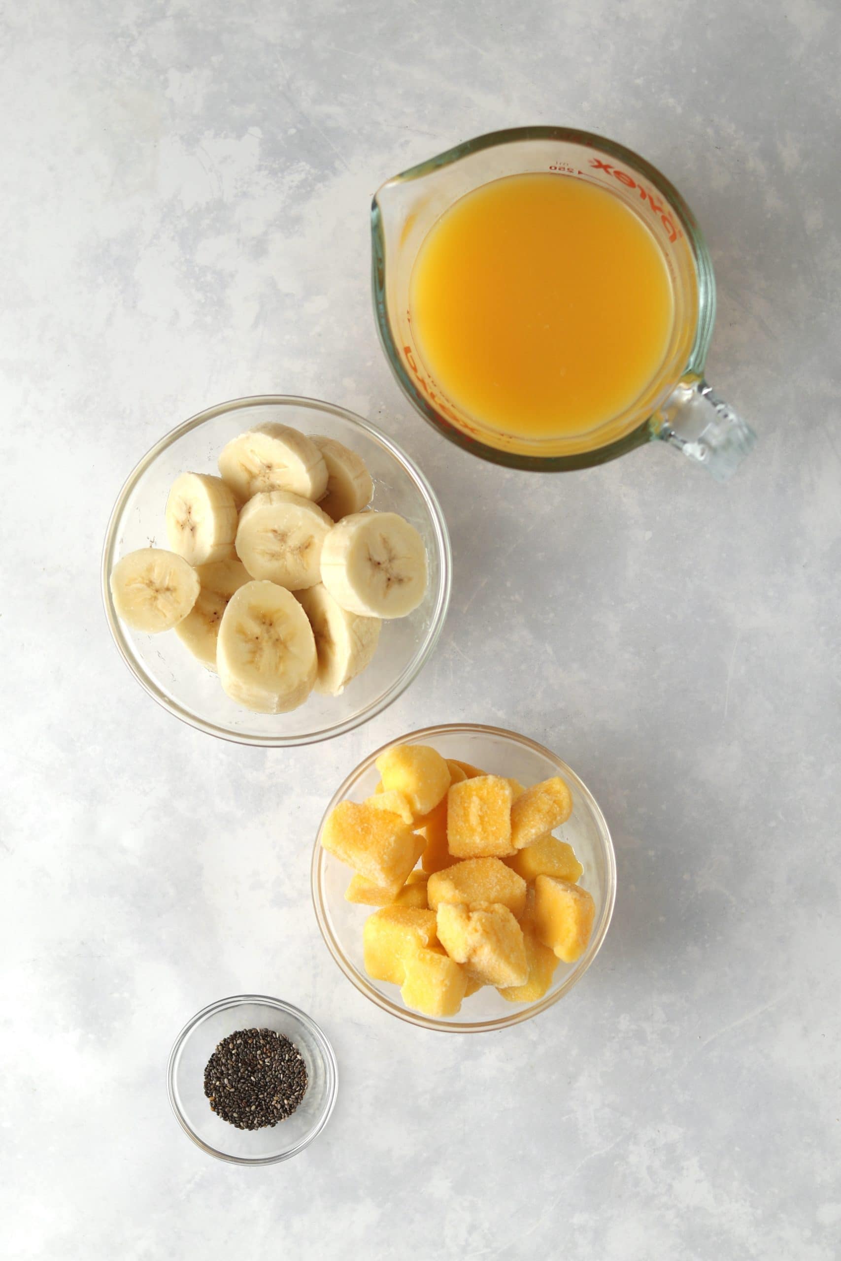 Orange juice, sliced bananas, diced mango, and chia seeds in bowls