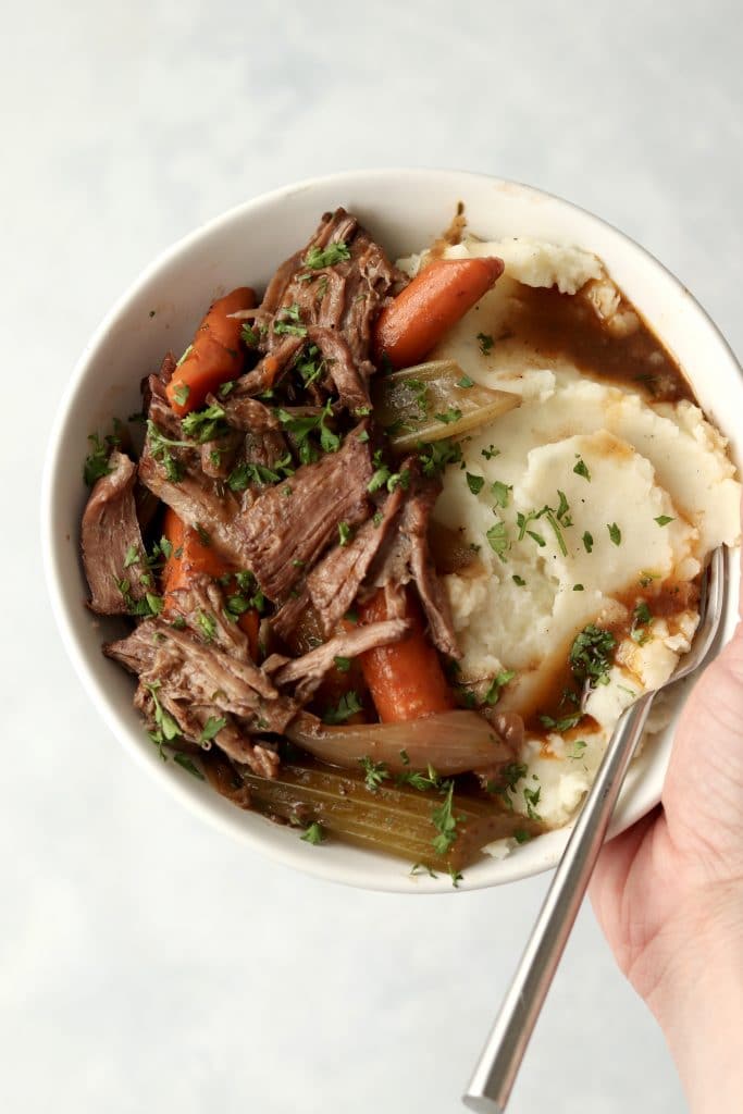 hand holding bowl of pot roast and mashed potatoes