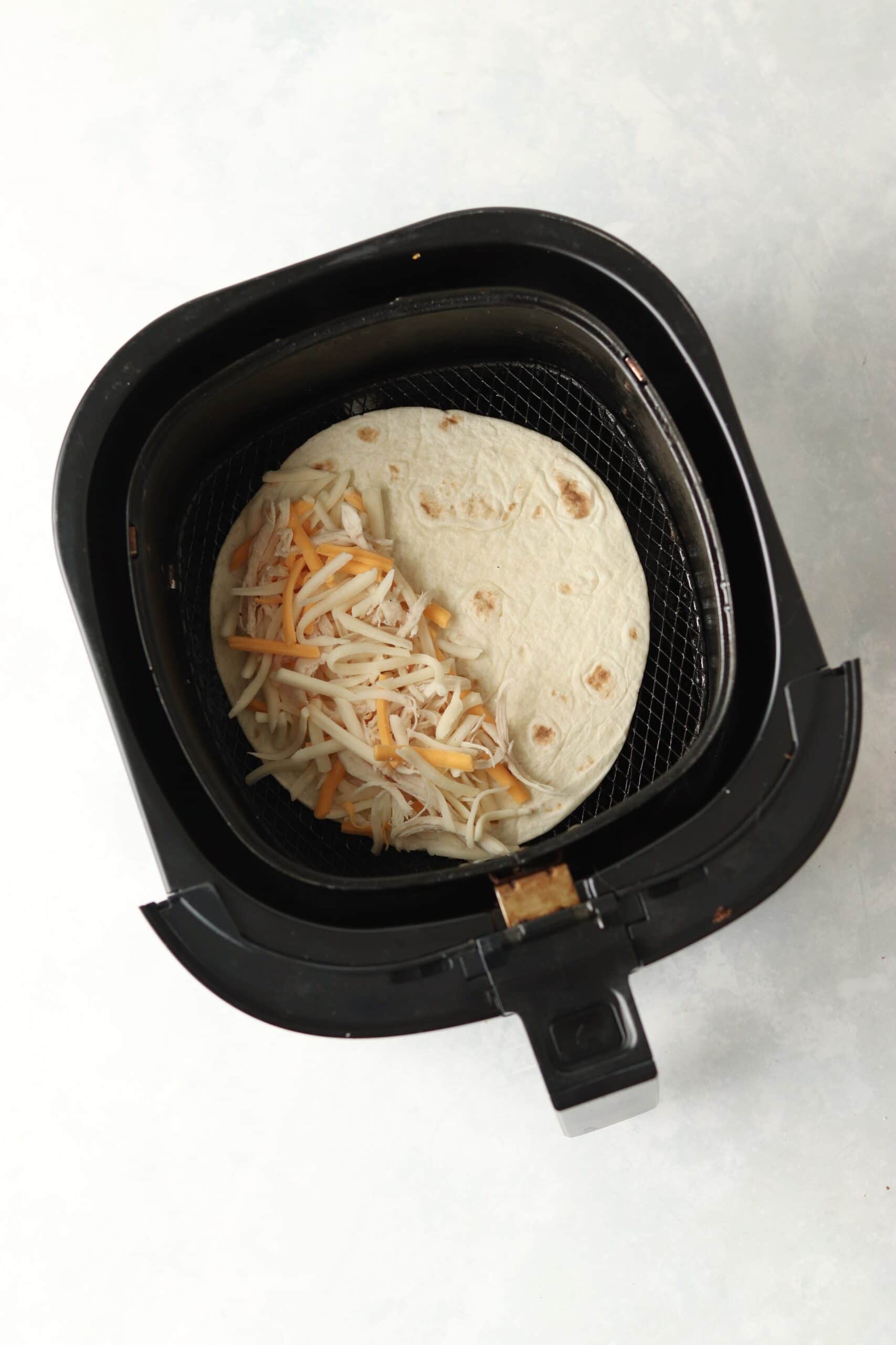 tortilla with shredded cheese in air fryer basket.
