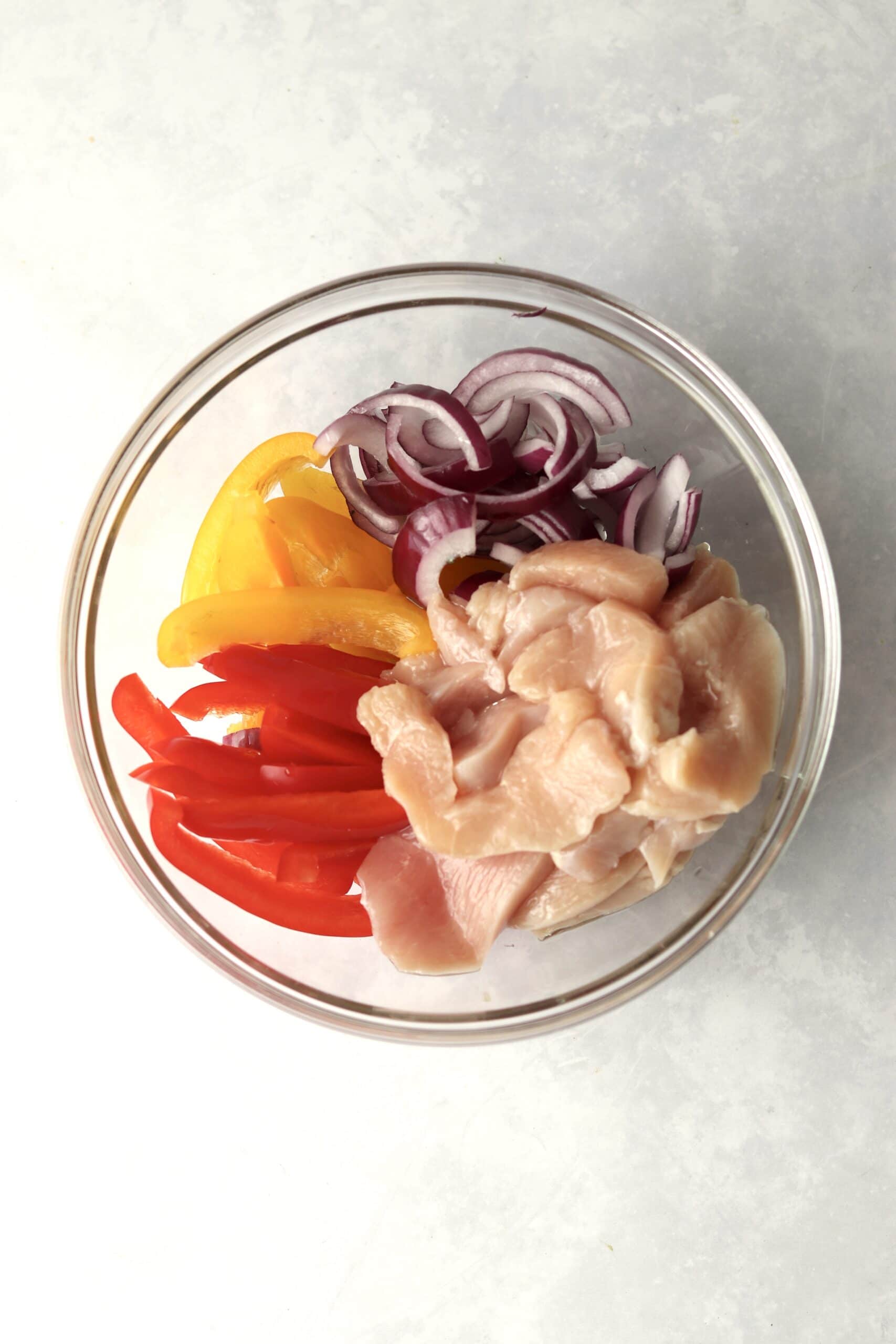 raw chicken, peppers, and onions in a bowl