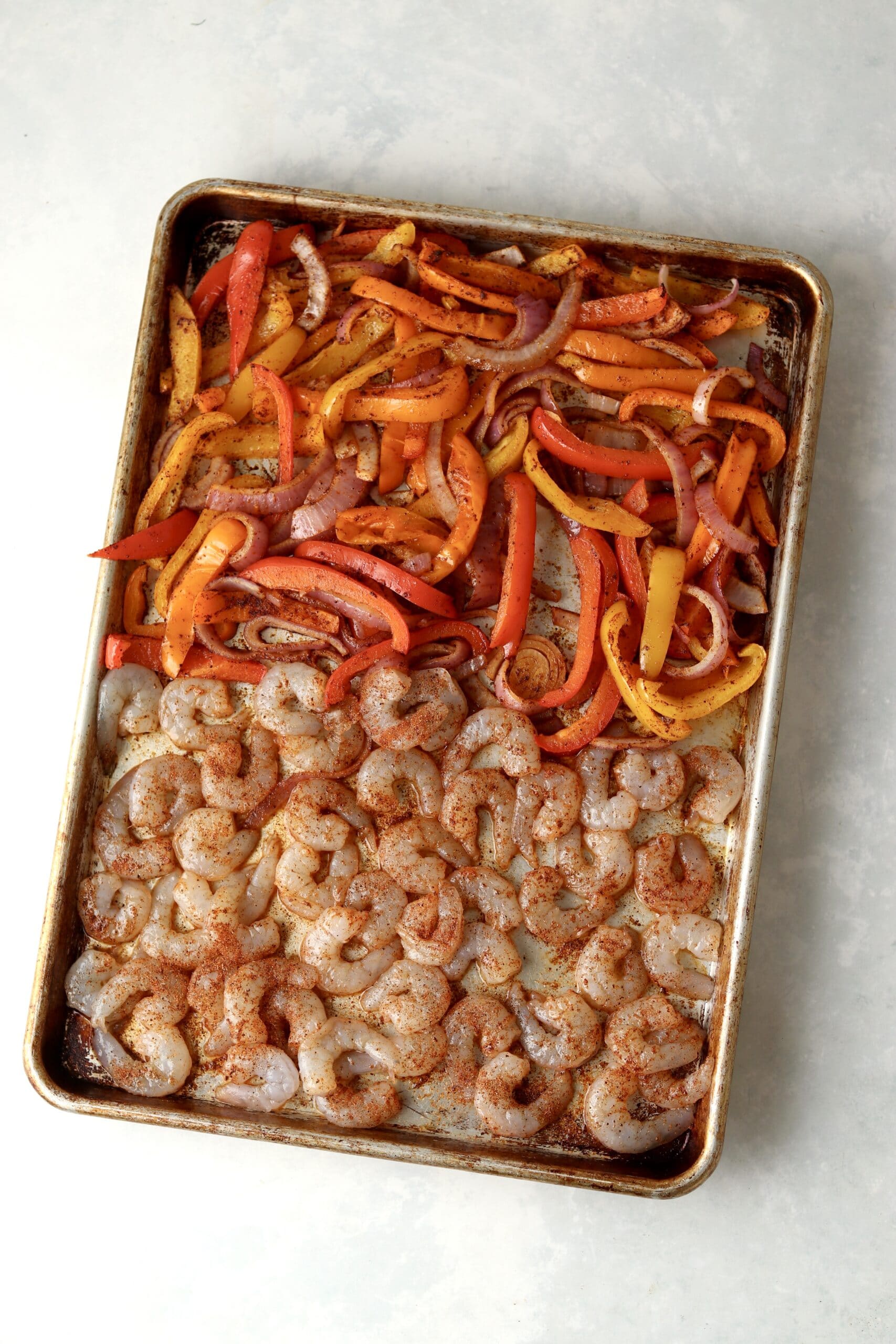raw shrimp with peppers and onions on sheet pan