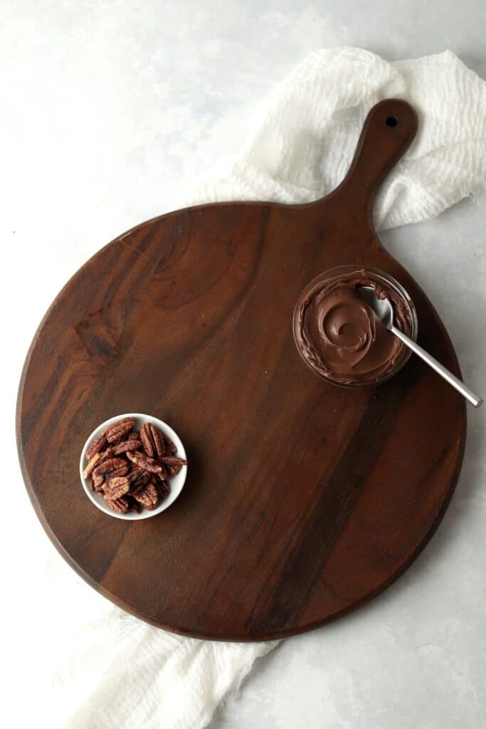 Bowl of chocolate spread and candied pecans on wooden board