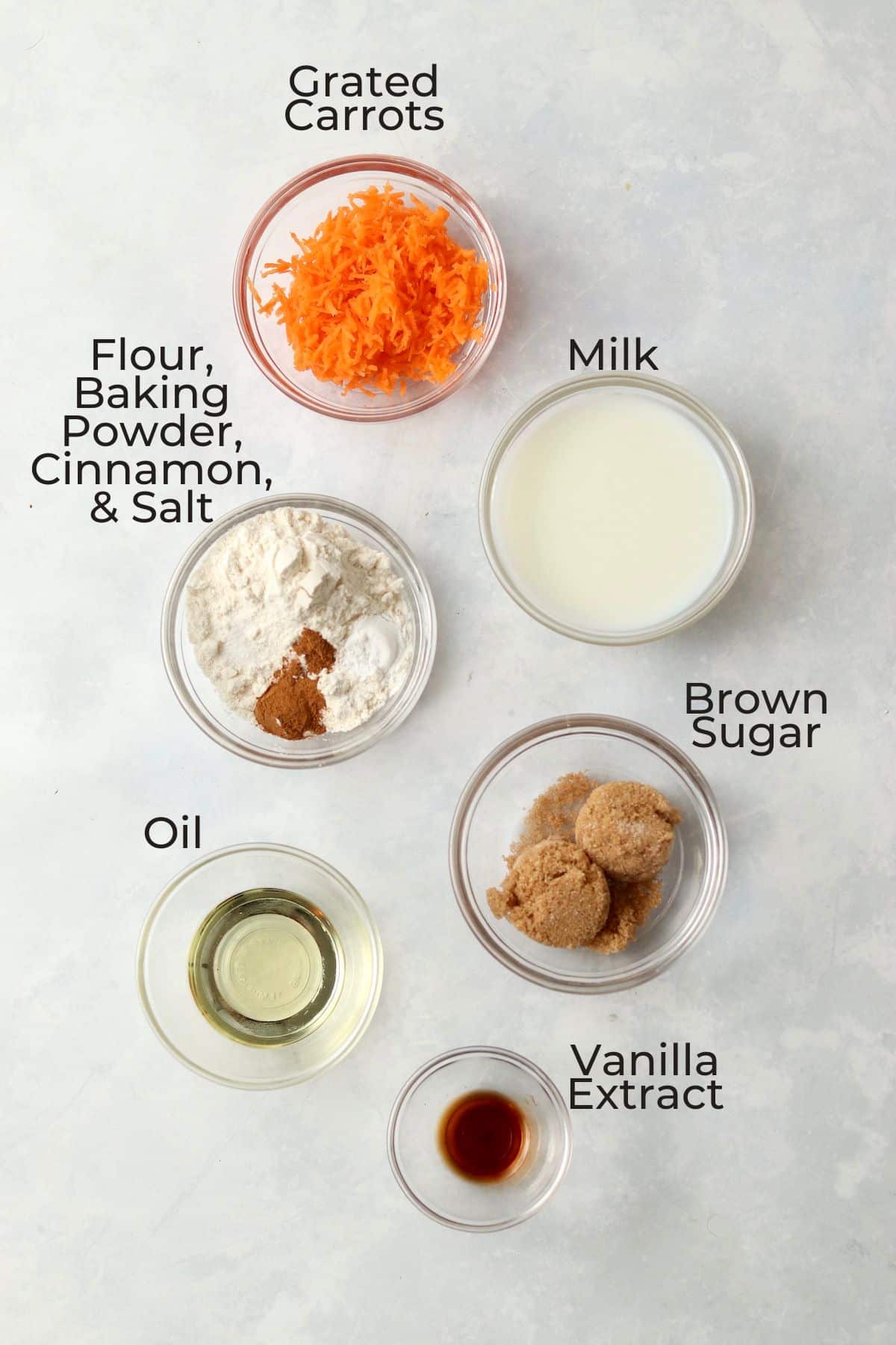 grated carrots, milk, flour, baking powder, cinnamon, oil, brown sugar, and vanilla extract in small bowls
