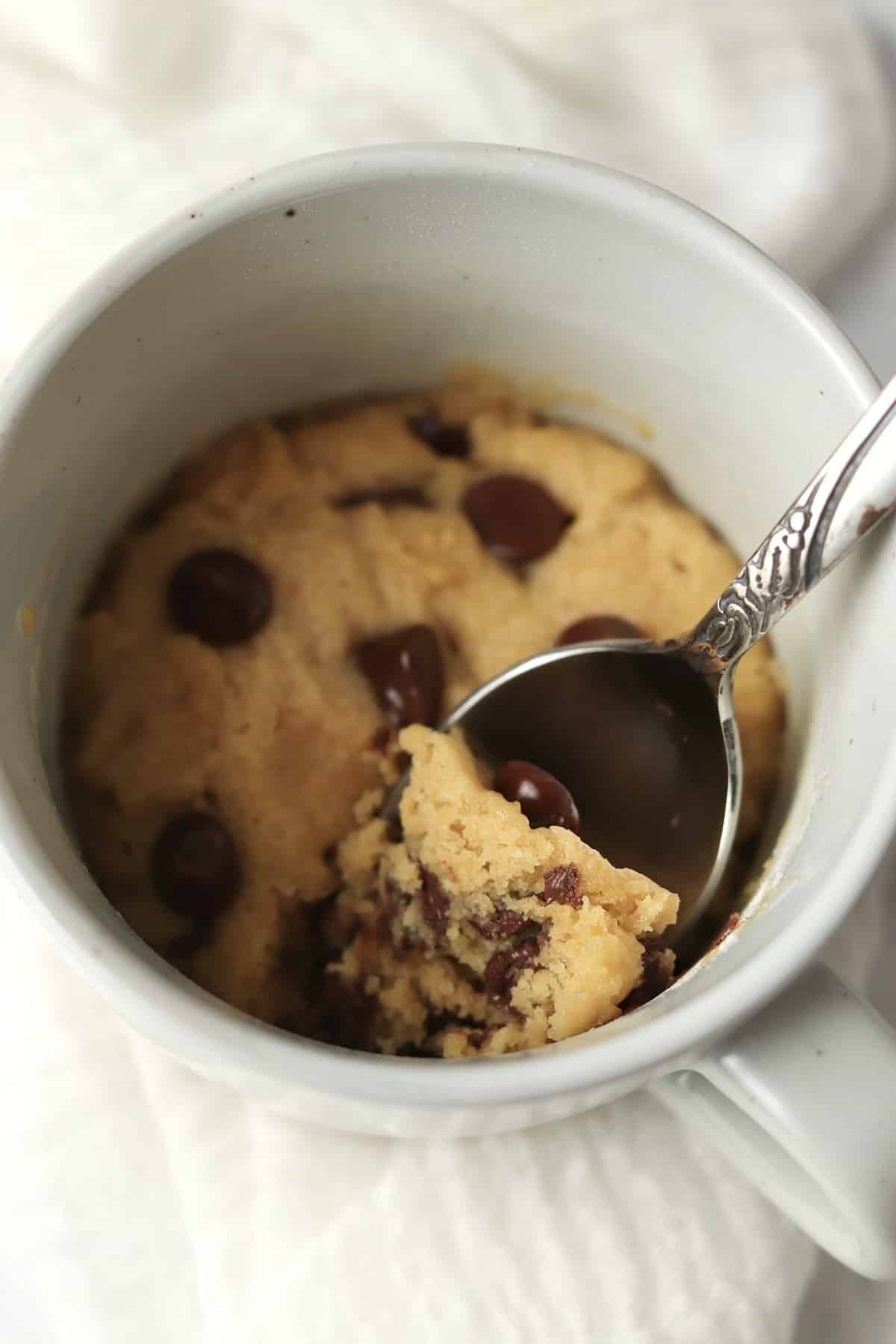close up of spoon dipping into mug chocolate chip cookie