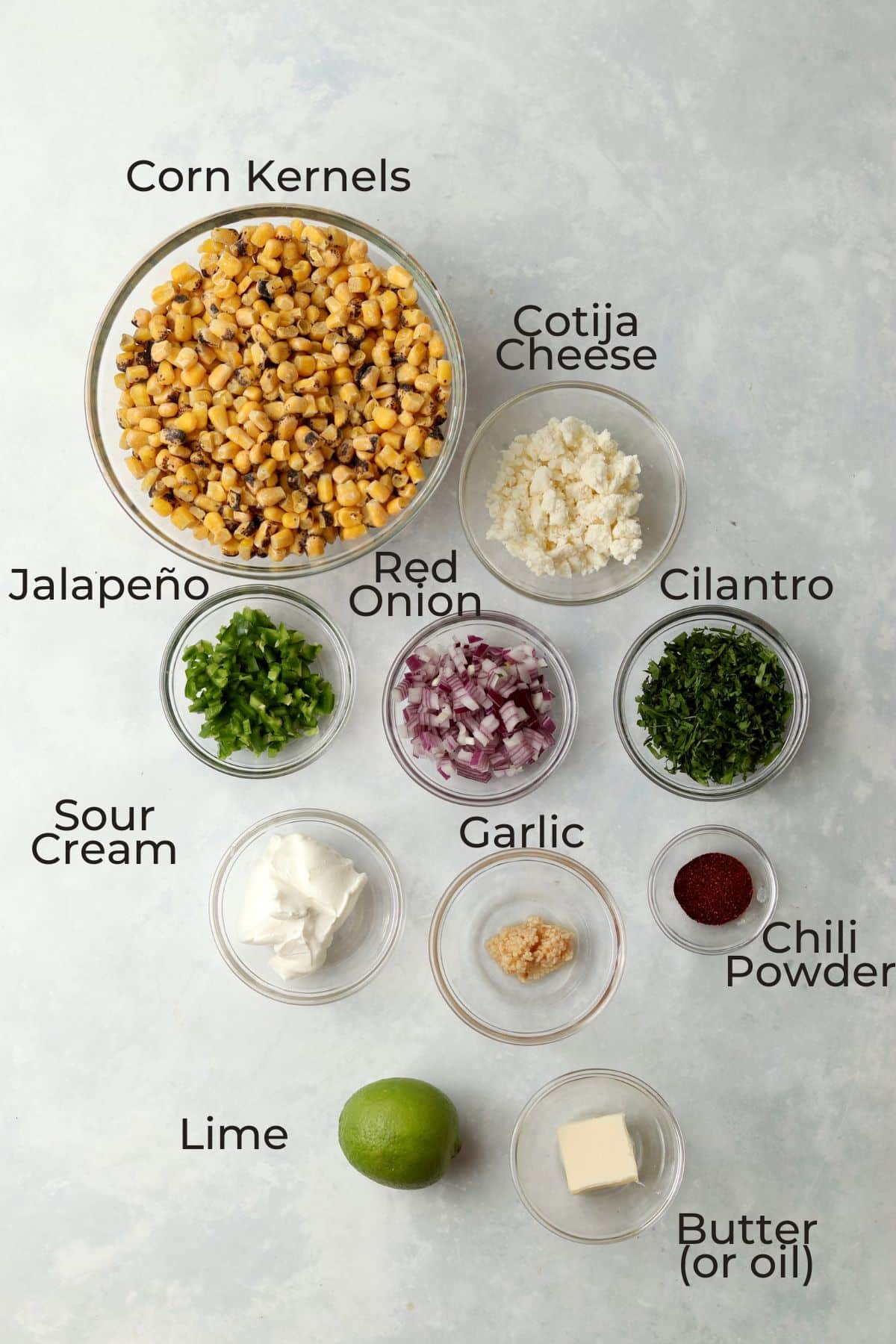 frozen corn kernels, cotija cheese, jalapeño, red onion, cilantro, sour cream, garlic, chili powder, and lime in prep bowls