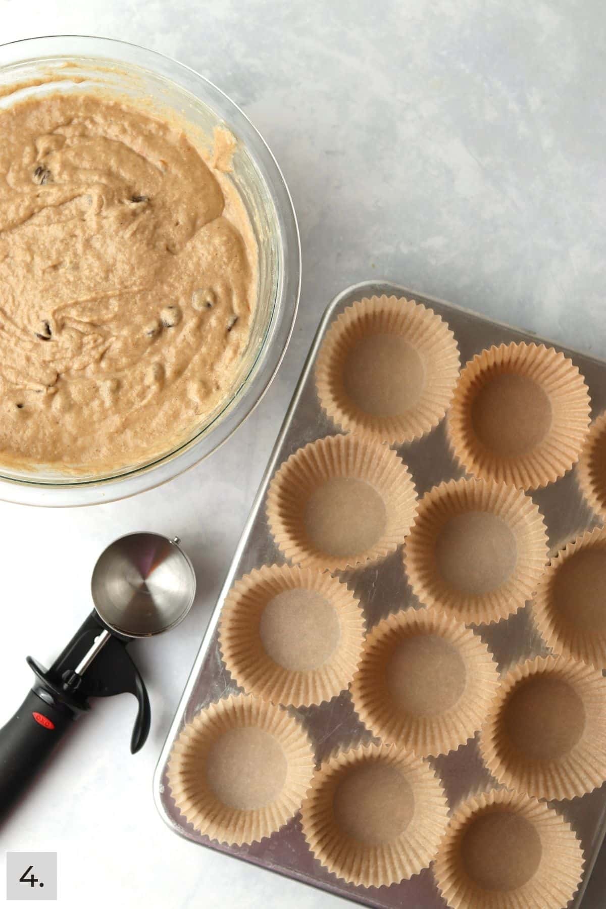 Muffin pan, scoop, and muffin batter in bowl.