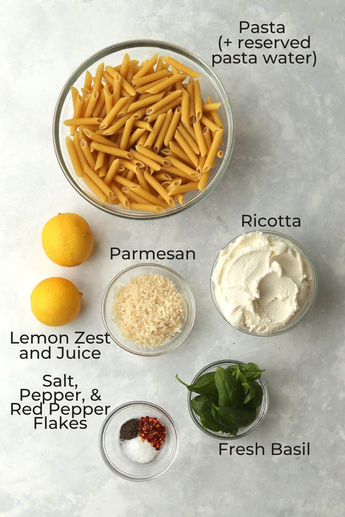 pasta, lemons, parmesan, ricotta, basil, and spices in glass bowls.