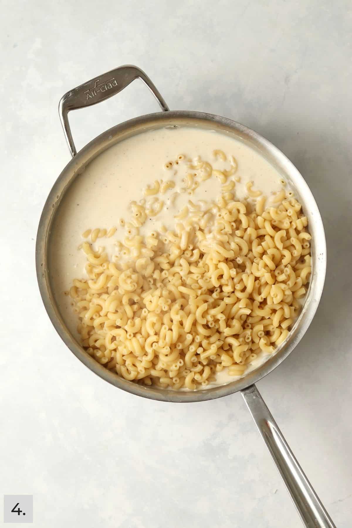 Macaroni noodles being added to white cheese sauce.