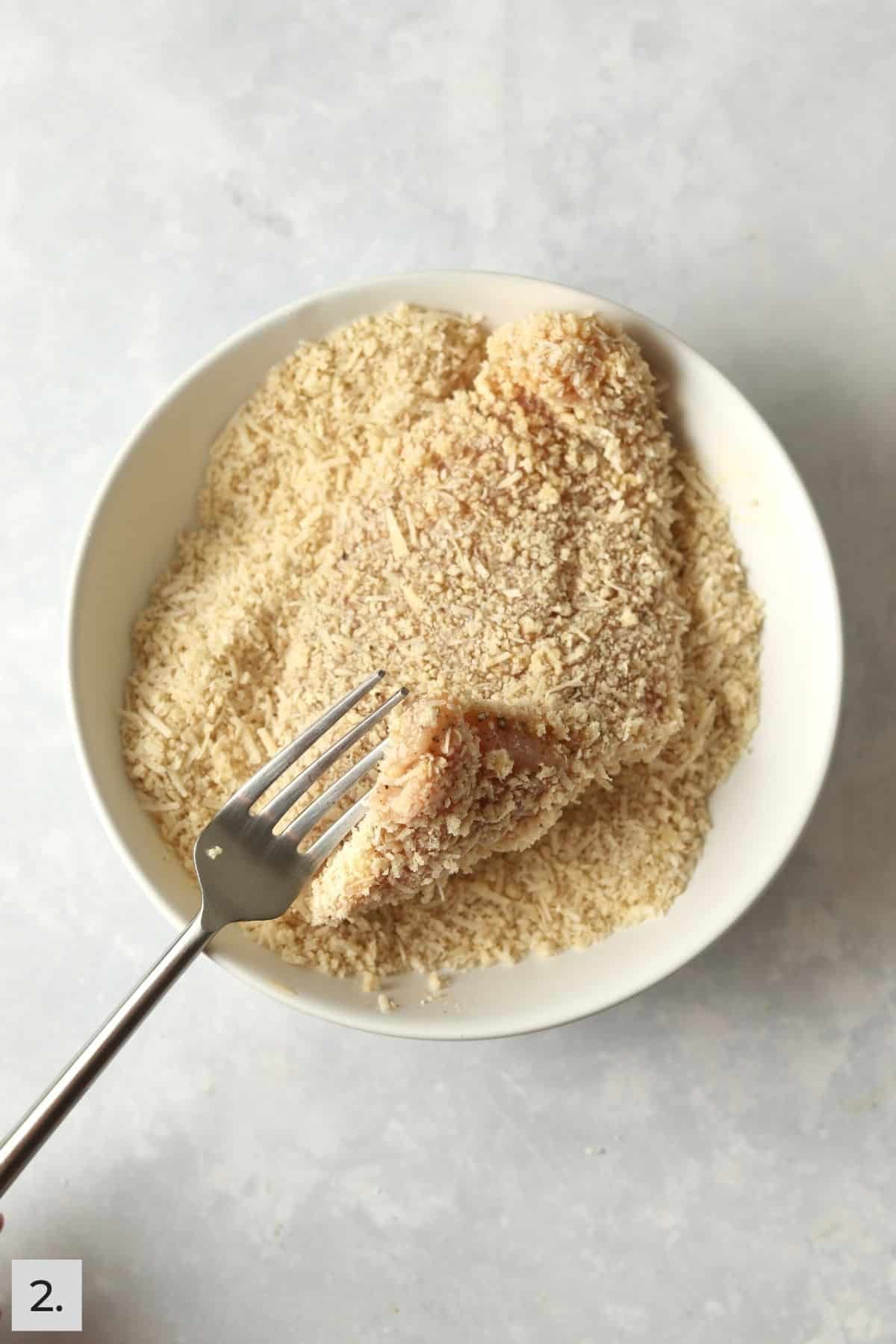 Piece of chicken being breaded in a parmesan mixture.