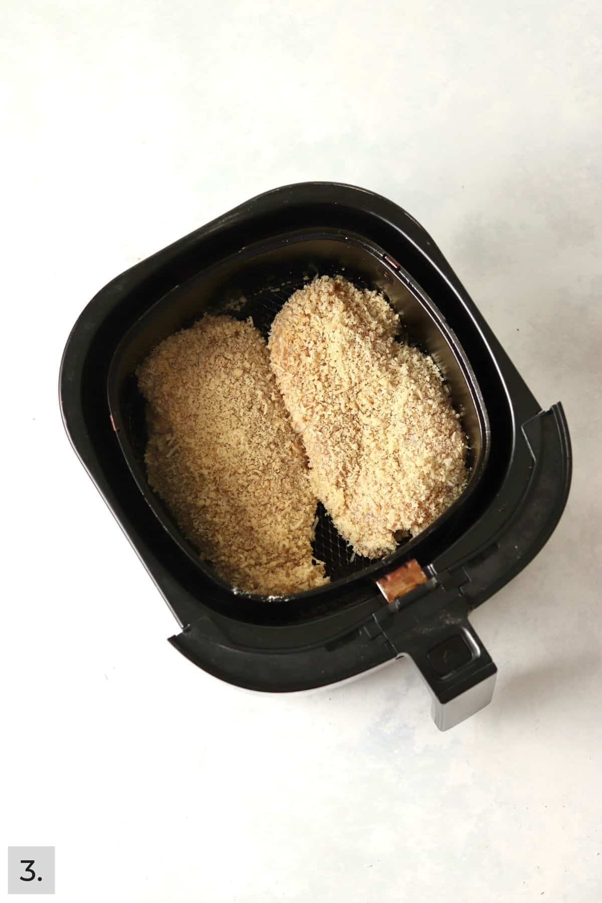 Uncooked parmesan crusted chicken in air fryer basket.