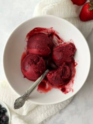 Scoops of mixed berry sorbet in a bowl with fresh berries.