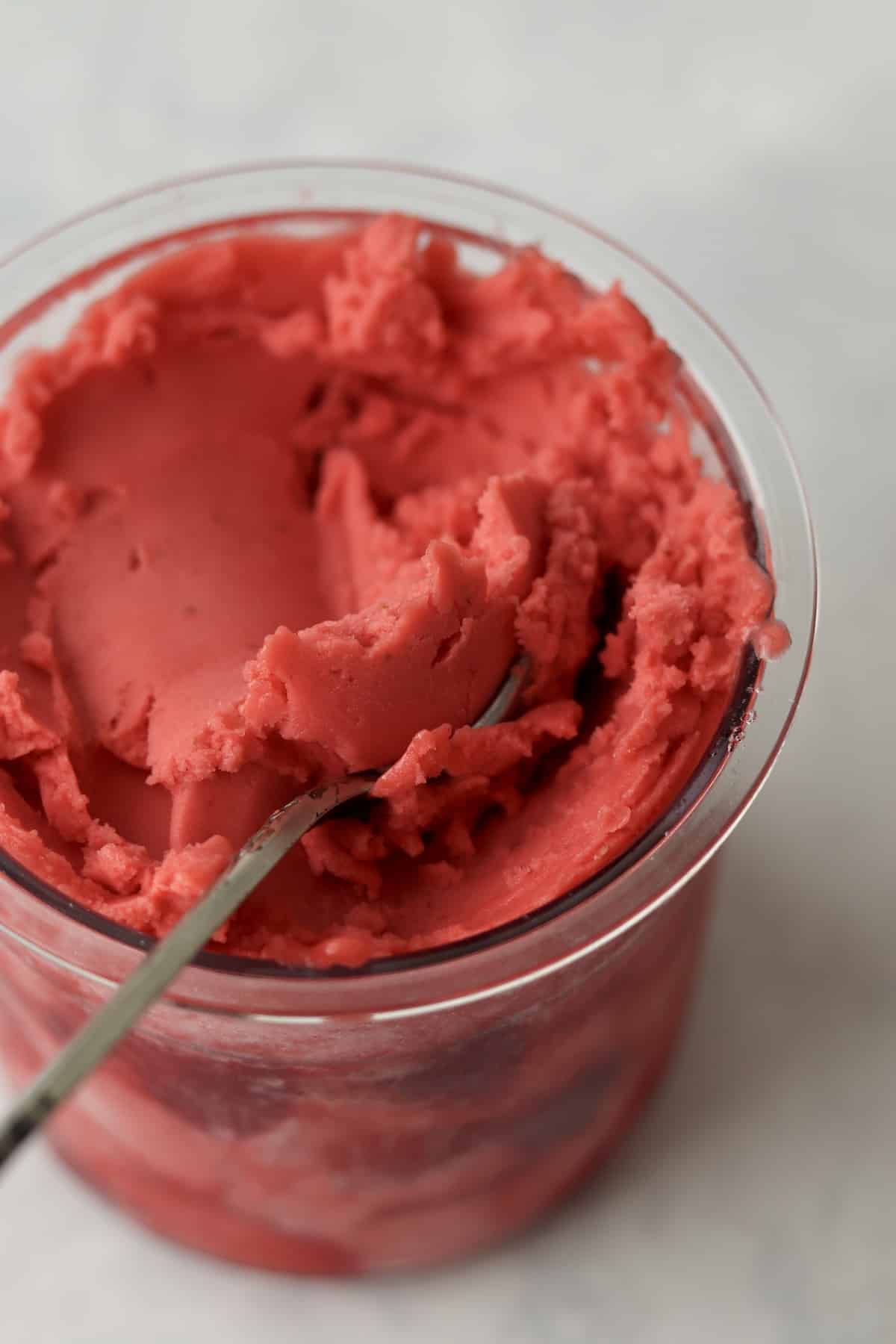 Creamy Ninja Creami strawberry sorbet in pint container with a spoon.