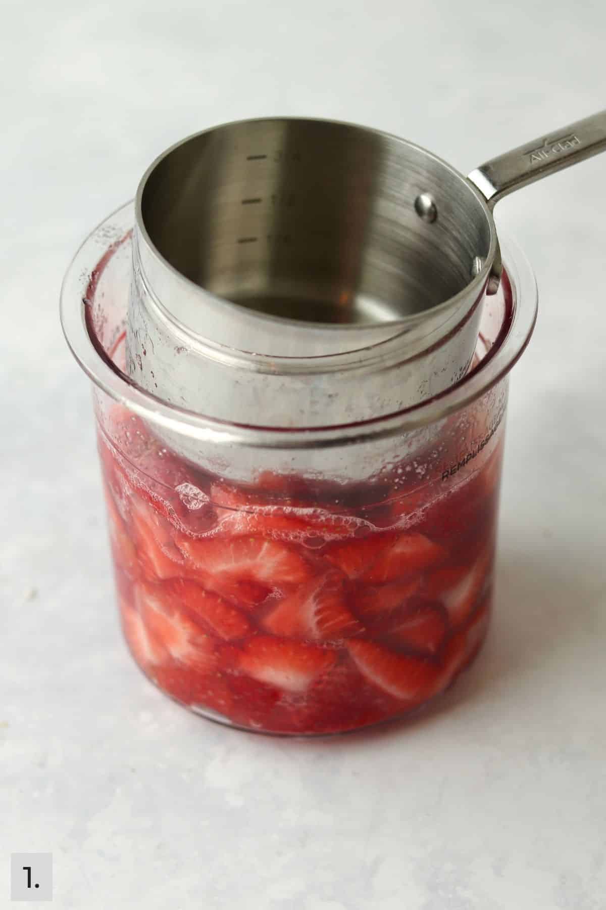 Metal measuring cup pressing down fresh strawberries in a Ninja Creami pint container.