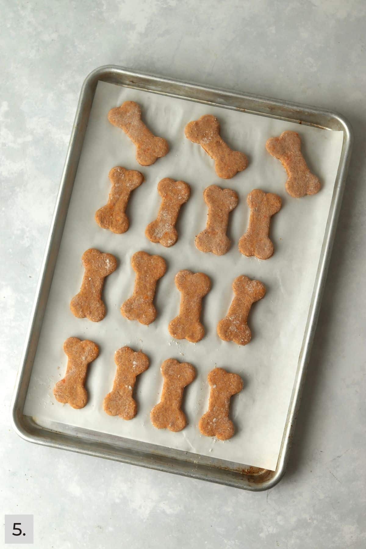 Unbaked sweet potato dog treats cut into bone shapes on a baking sheet.