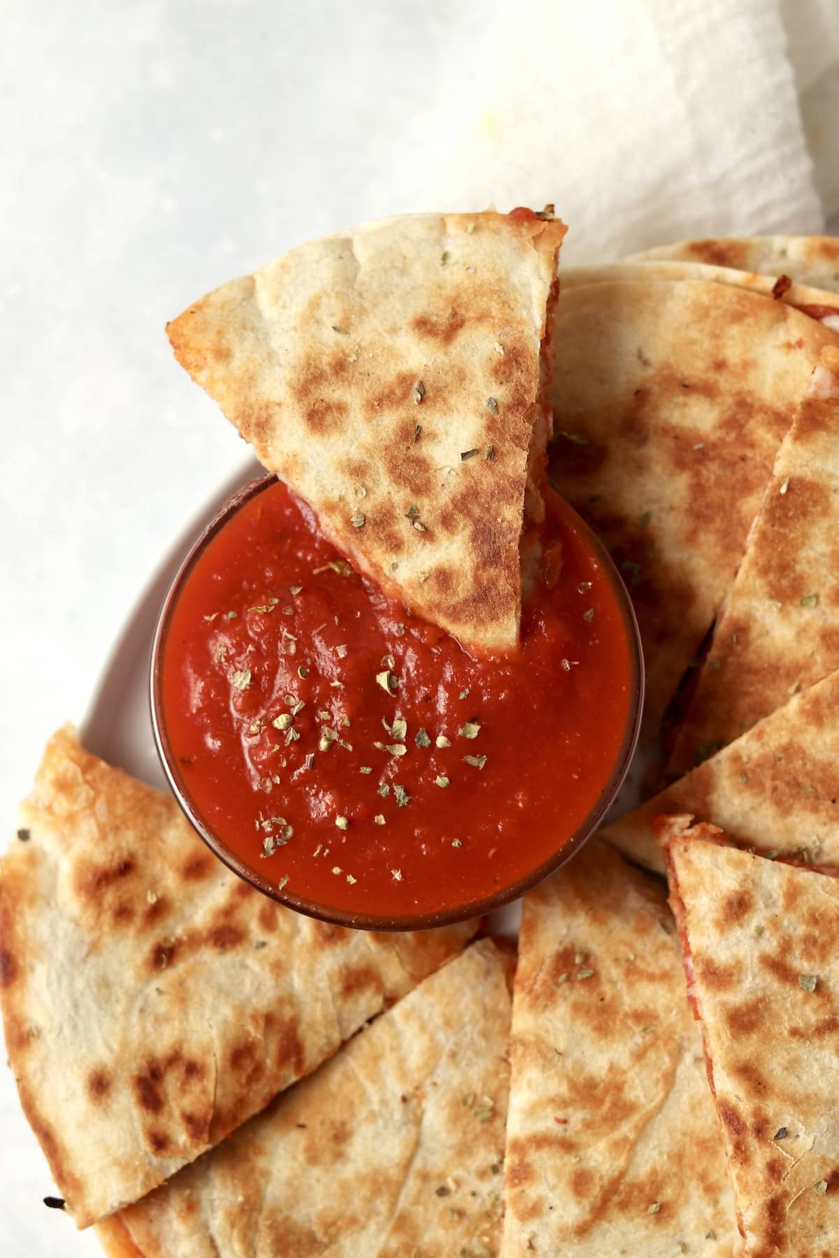 Blackstone pizza quesadilla being dipped in a bowl of marinara sauce.