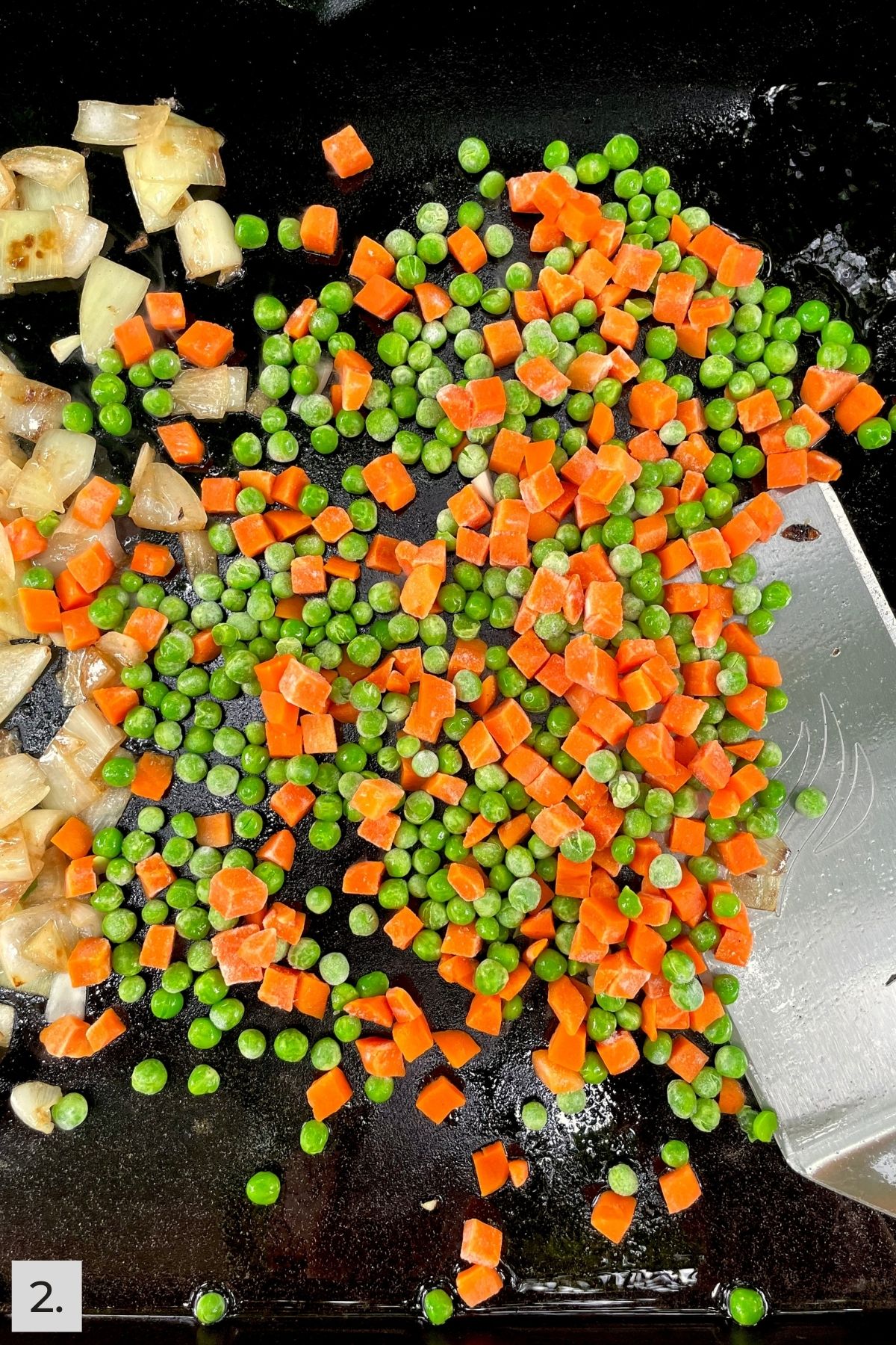 Frozen peas and carrots added to Blackstone griddle with onions.