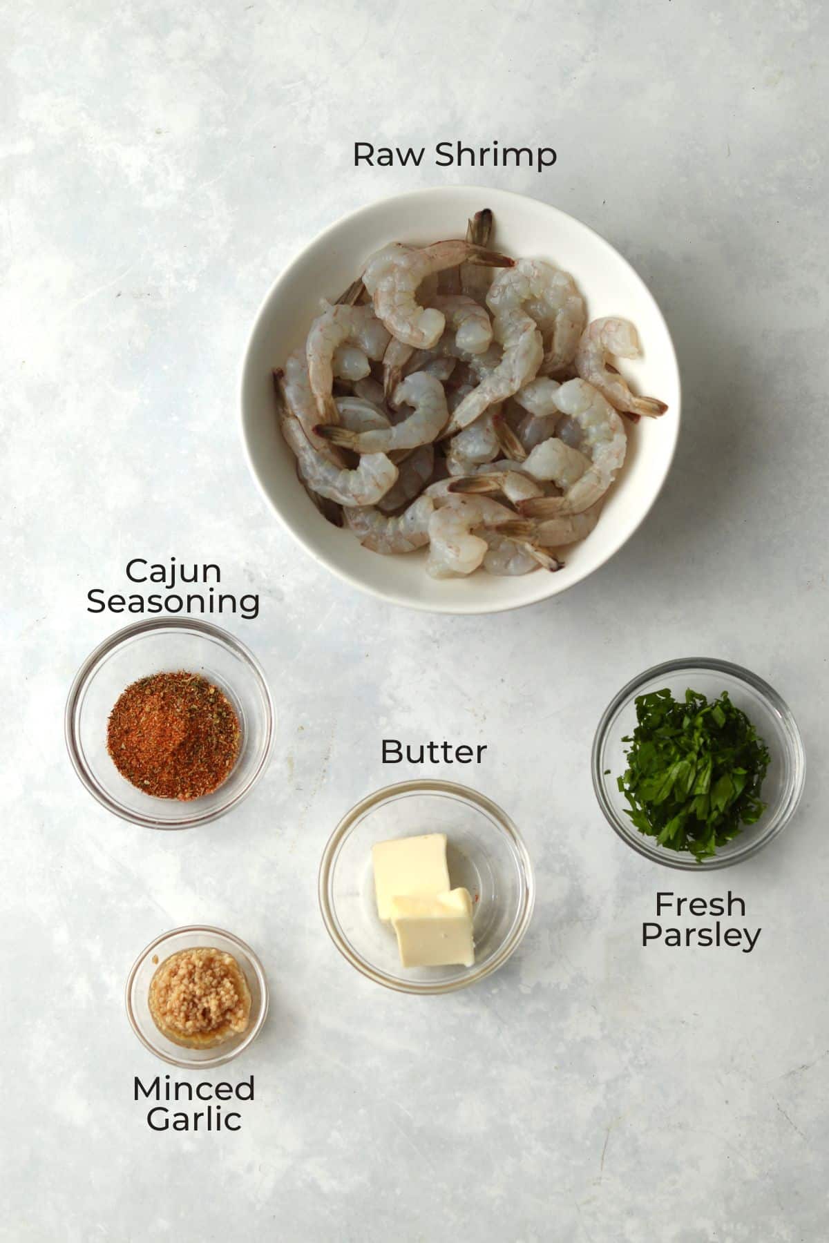 Shrimp, butter, garlic, cajun seasoning, and parsley in glass bowls.