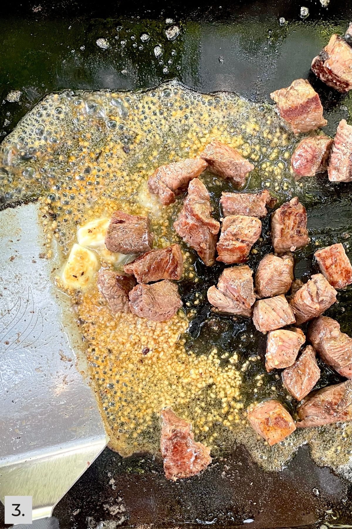 Steak bites being tossed in garlic butter on flat top griddle.