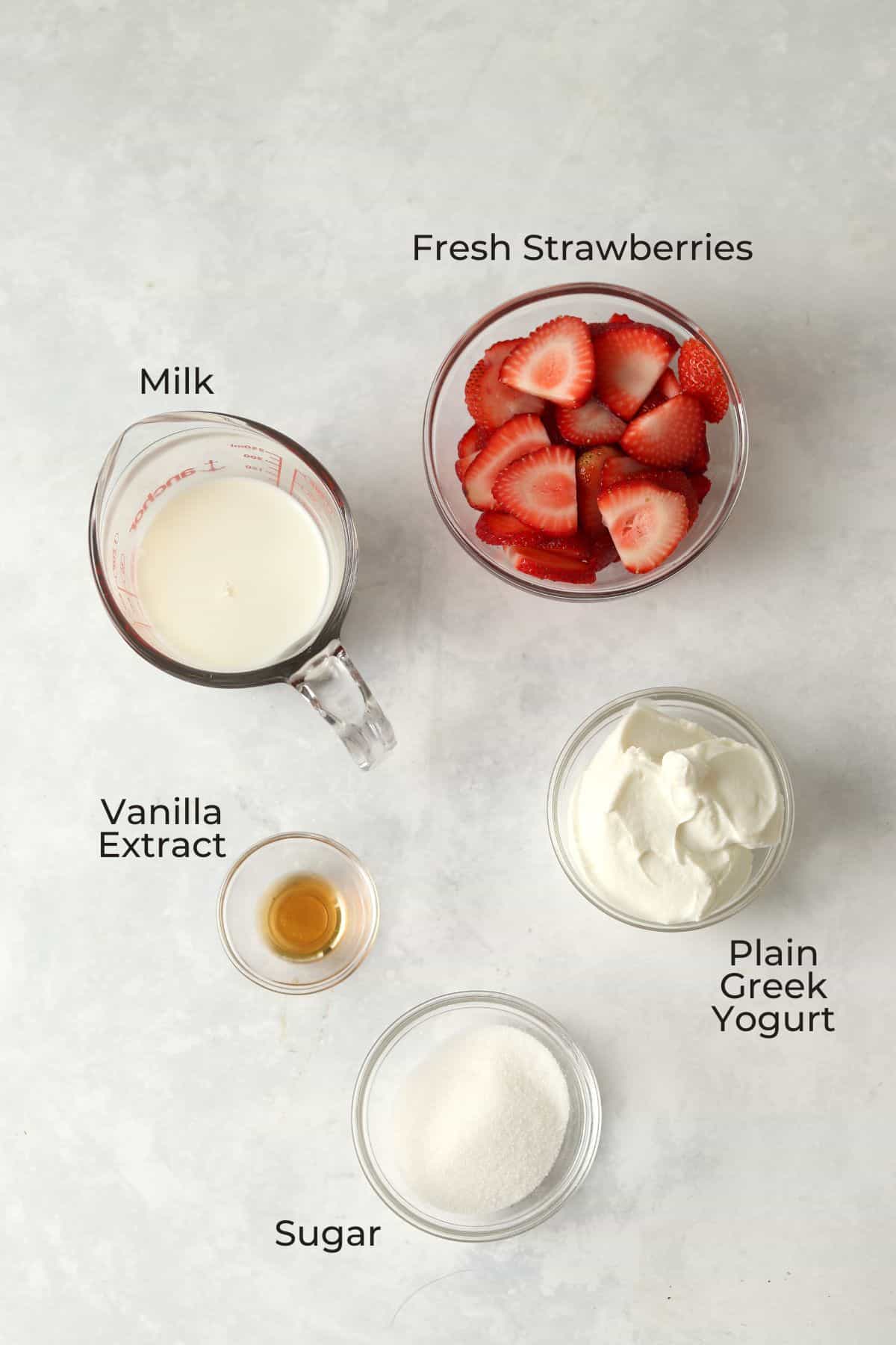 Strawberries, milk, Greek yogurt, sugar, and vanilla in glass prep bowls.