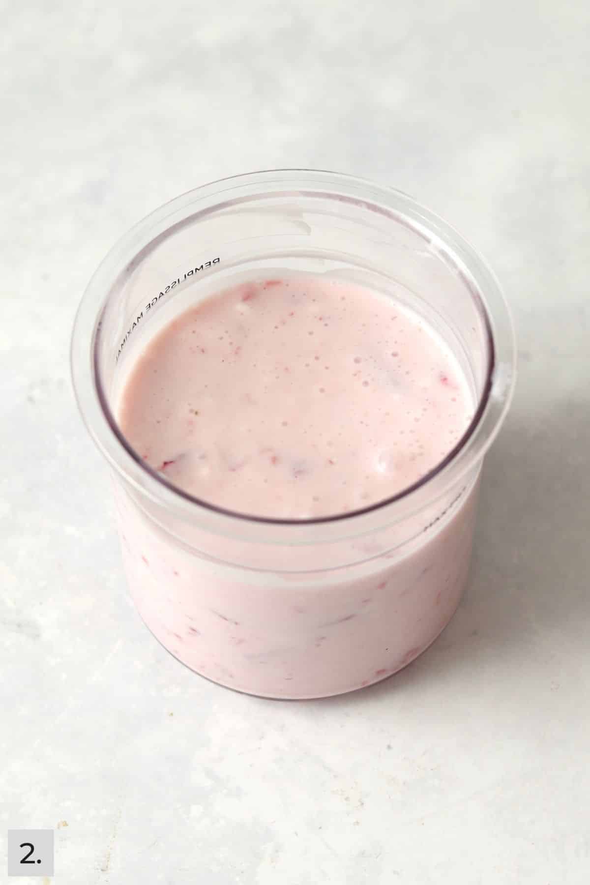 Greek yogurt and milk mixed with crushed strawberries in a Ninja Creami pint container.