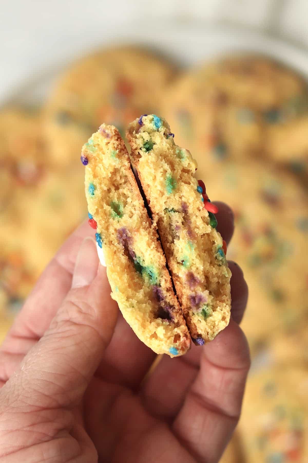 Hand holding up a funfetti cake mix cookie that is broken in half to show inside.