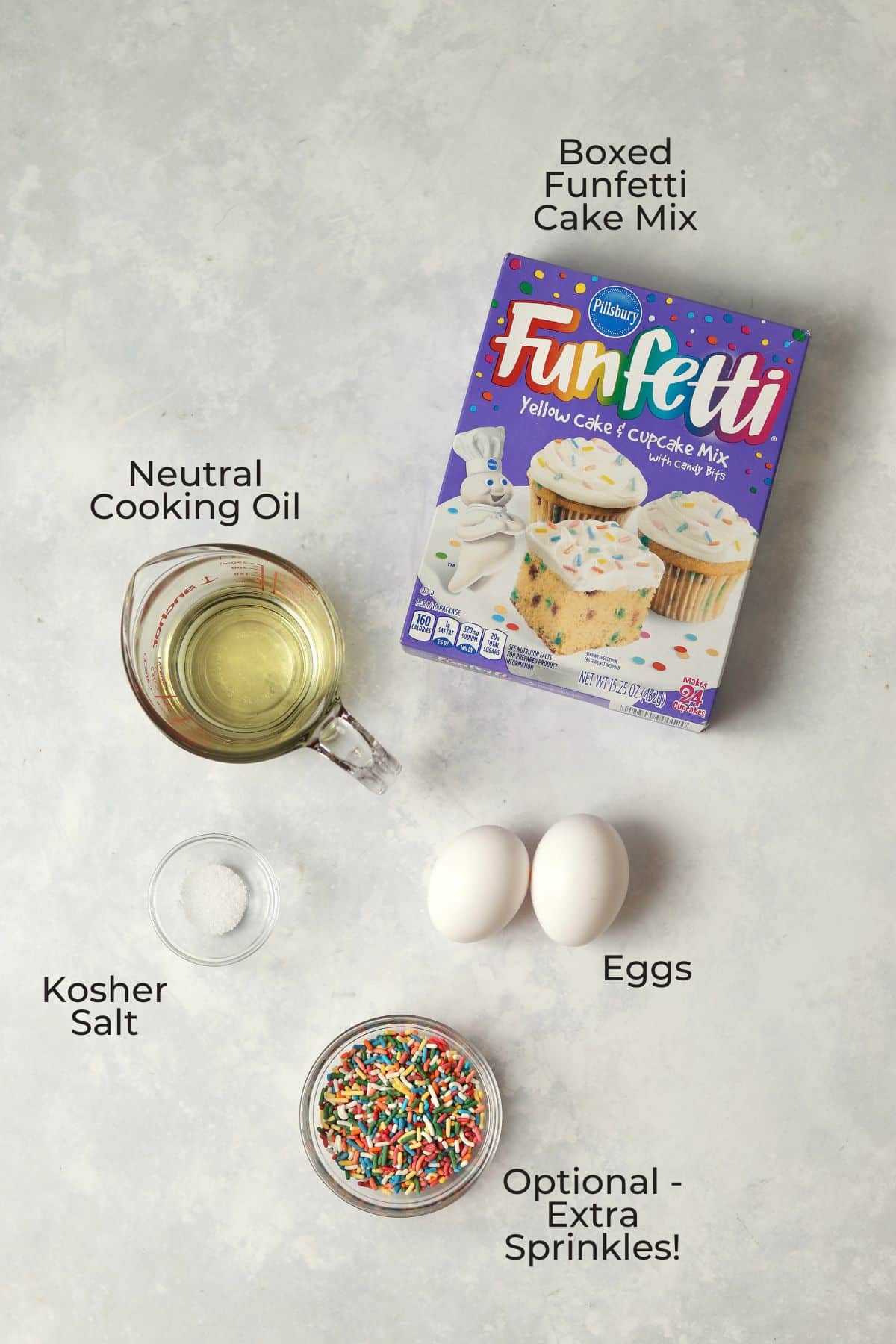 Boxed funfetti cake mix, oil in a measuring cup, two eggs, and small bowls with salt and sprinkles.