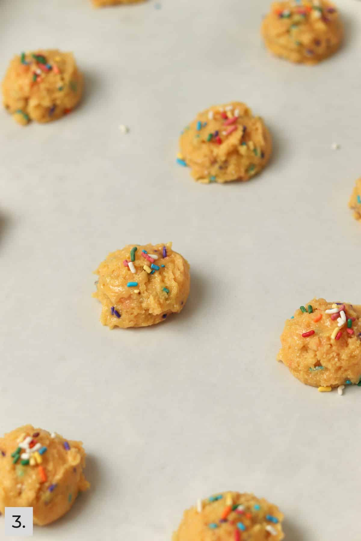 Funfetti cake mix cookie dough balls on sheet pan with sprinkles on top.