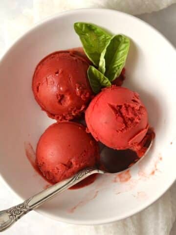 Scoops of Ninja Creami Strawberry Basil Sorbet in a bowl with fresh basil leaves.