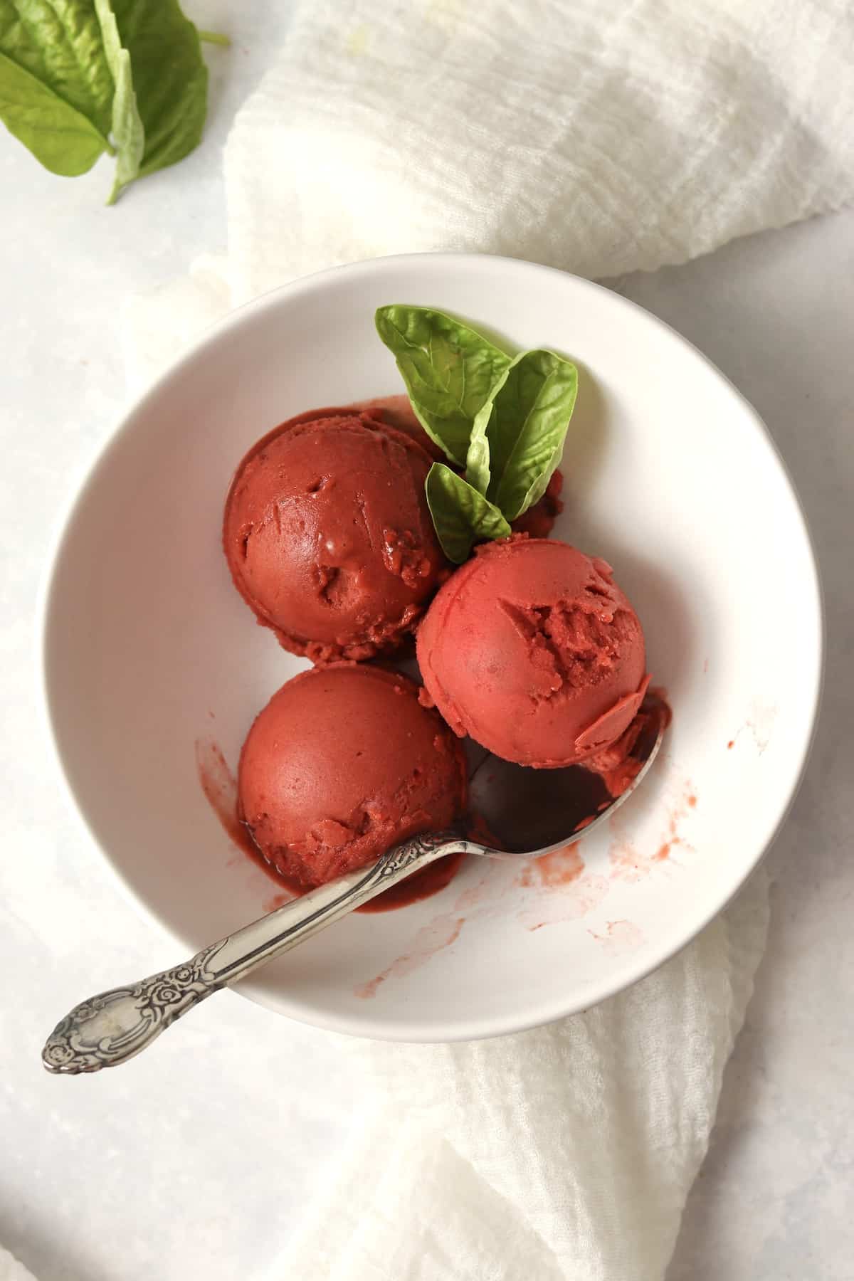 Scoops of Ninja Creami Strawberry Basil Sorbet in a bowl with fresh basil leaves.