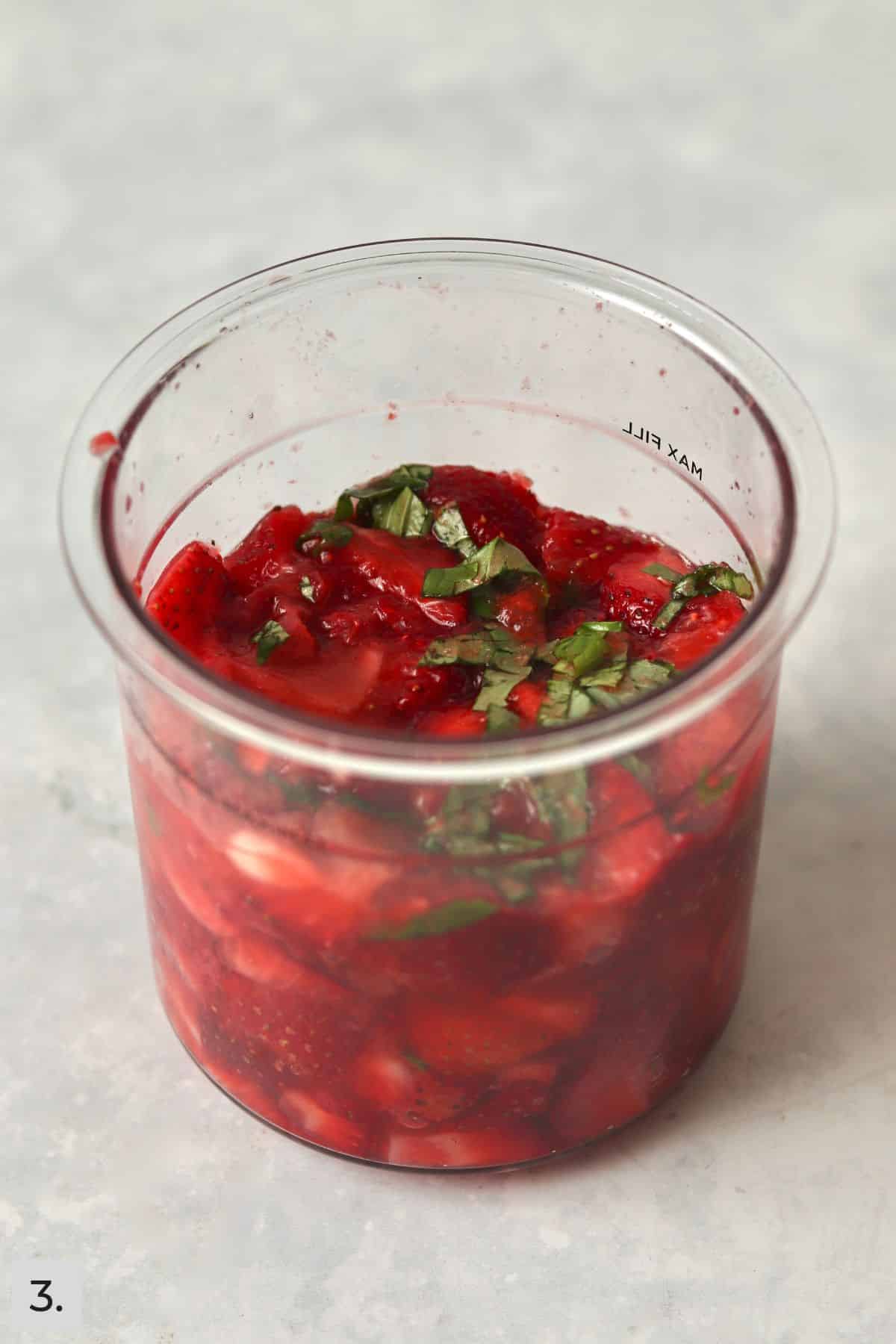 Basil mixed into fresh strawberries in pint container.