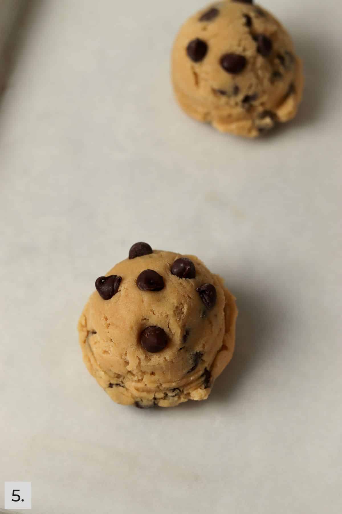 Two chocolate chip cookie dough balls on a small sheet pan.